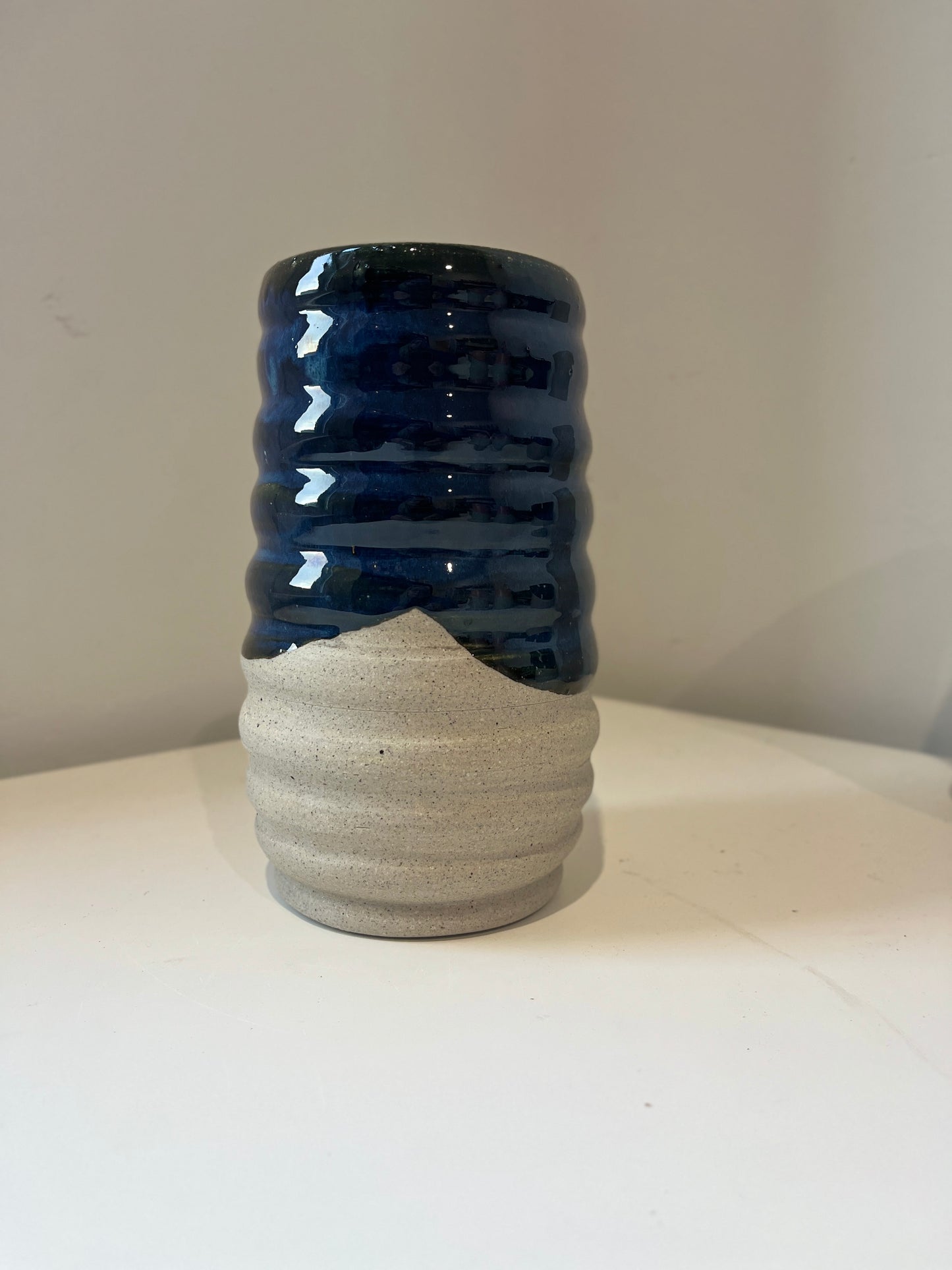 Ceramic vase glazed in dark blue and raw gray speckled clay on a white background.