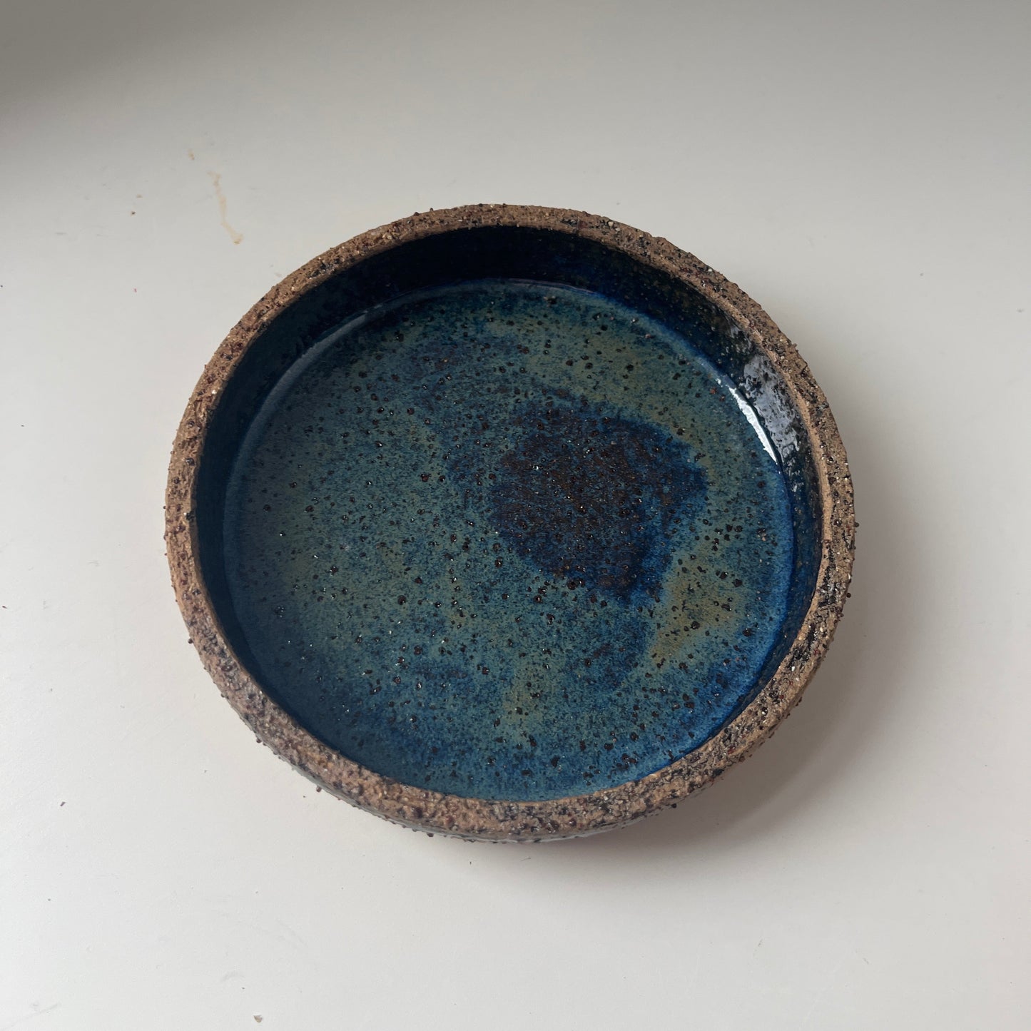 Ceramic saucer with blue glaze and brown rim on a white background