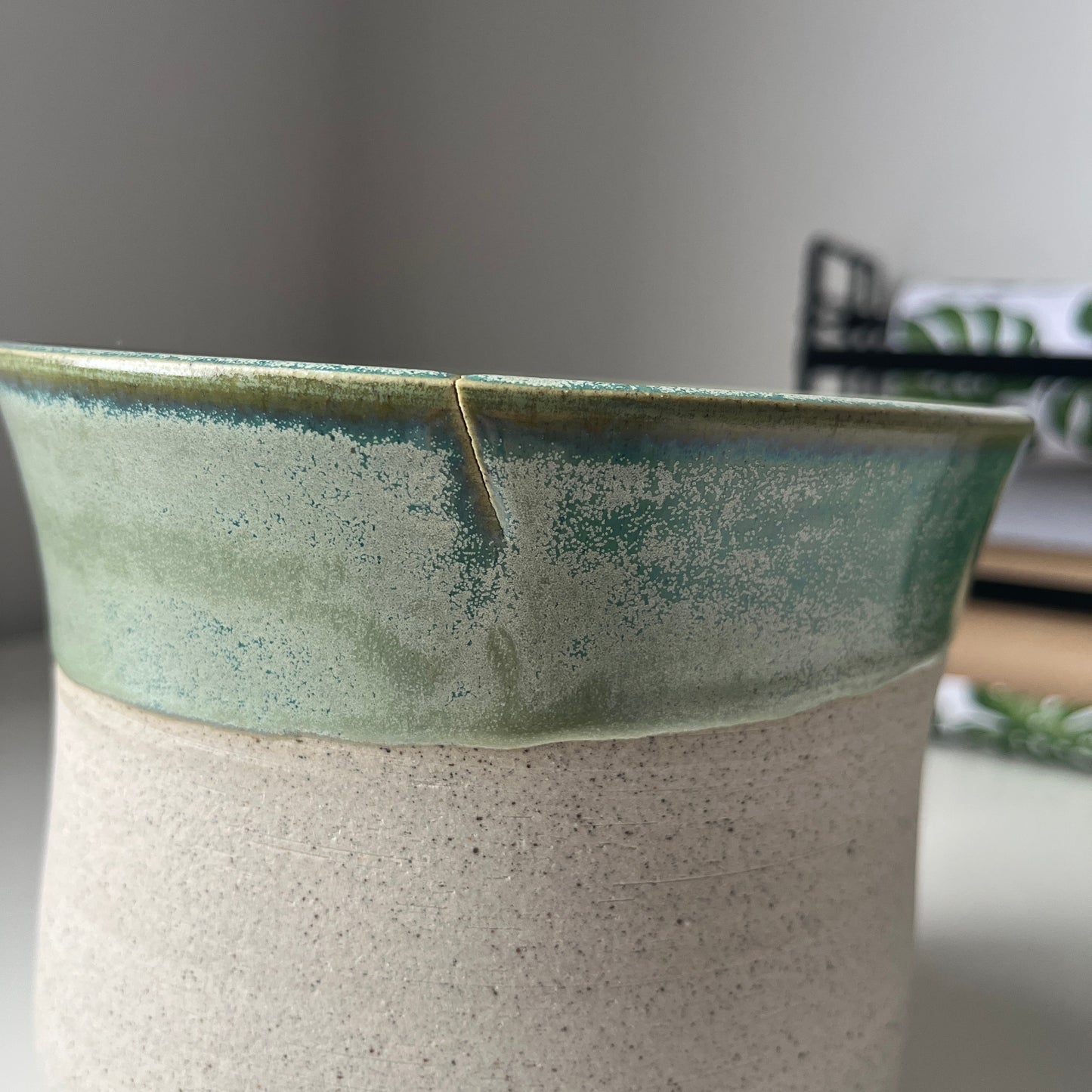 Close-up of a ceramic vase with a greenish glaze and a small crack in rim.