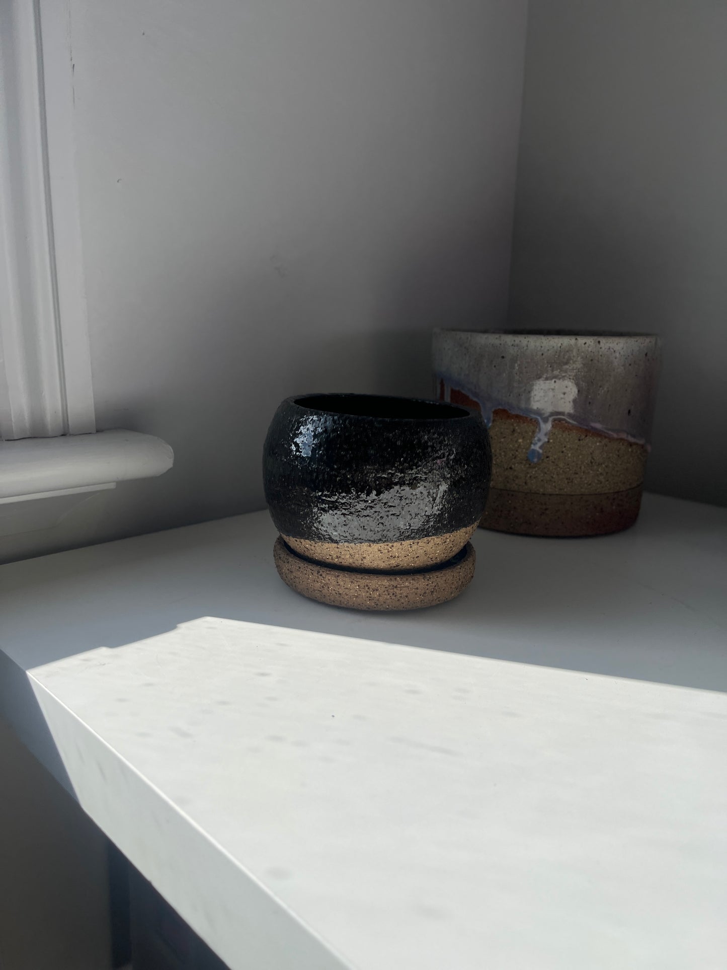 Two ceramic pots on a white surface with a neutral background