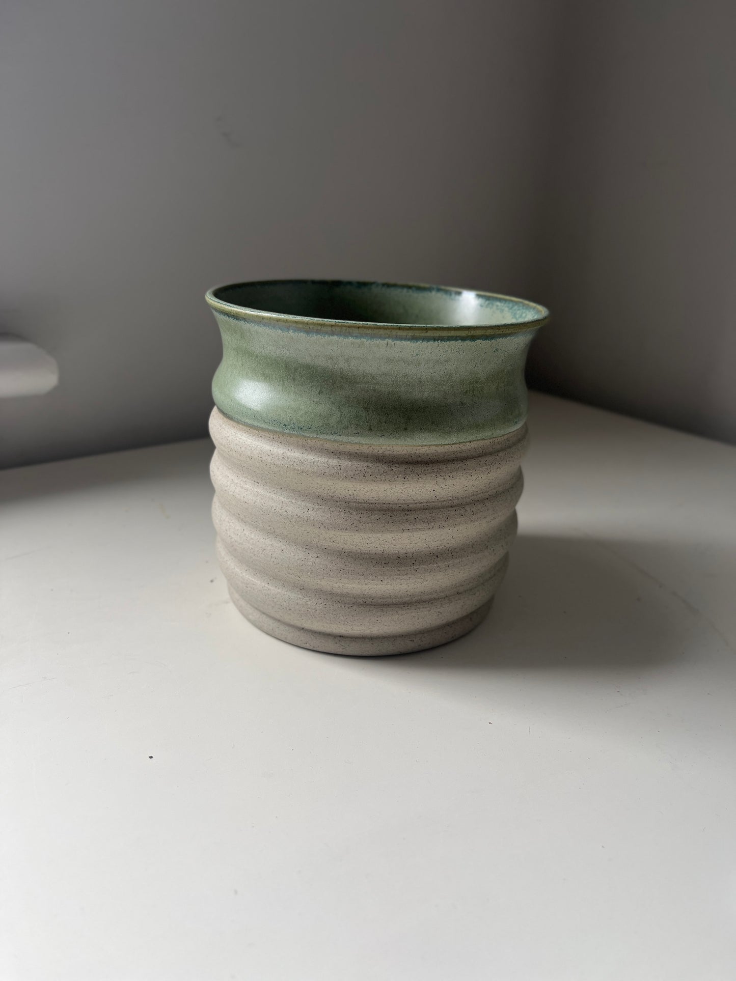 Green ceramic vase on a white surface with a gray background