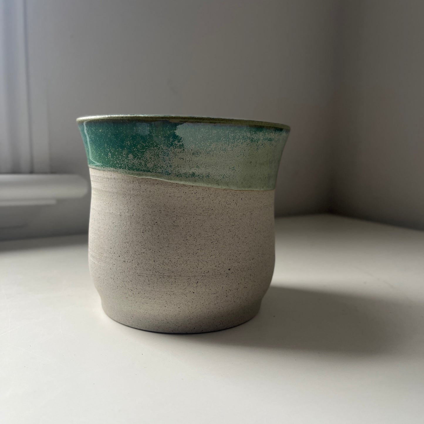 Ceramic planter with green top and raw bottom on a white surface