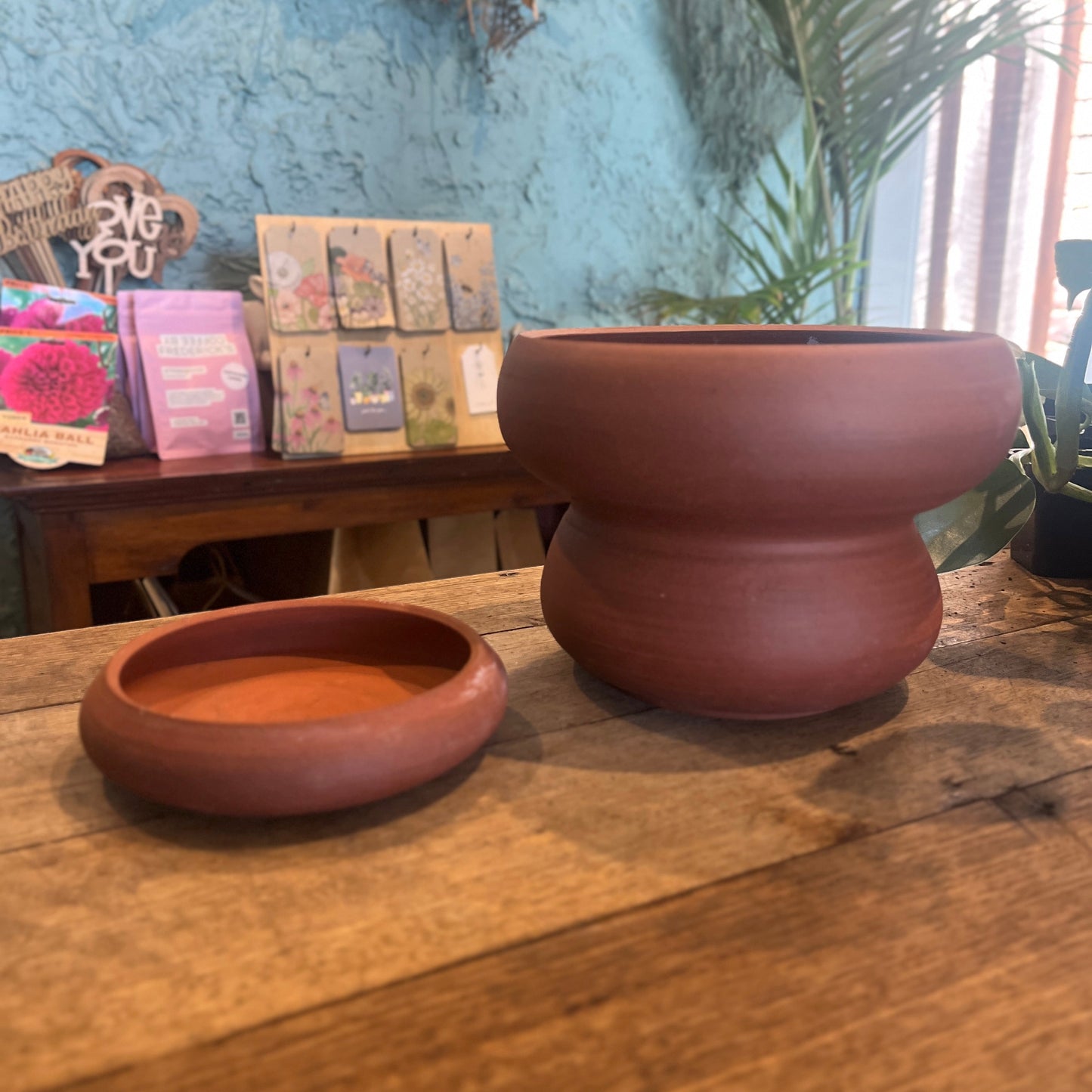 Terracotta pot on a wooden surface with a colorful card display in the background.