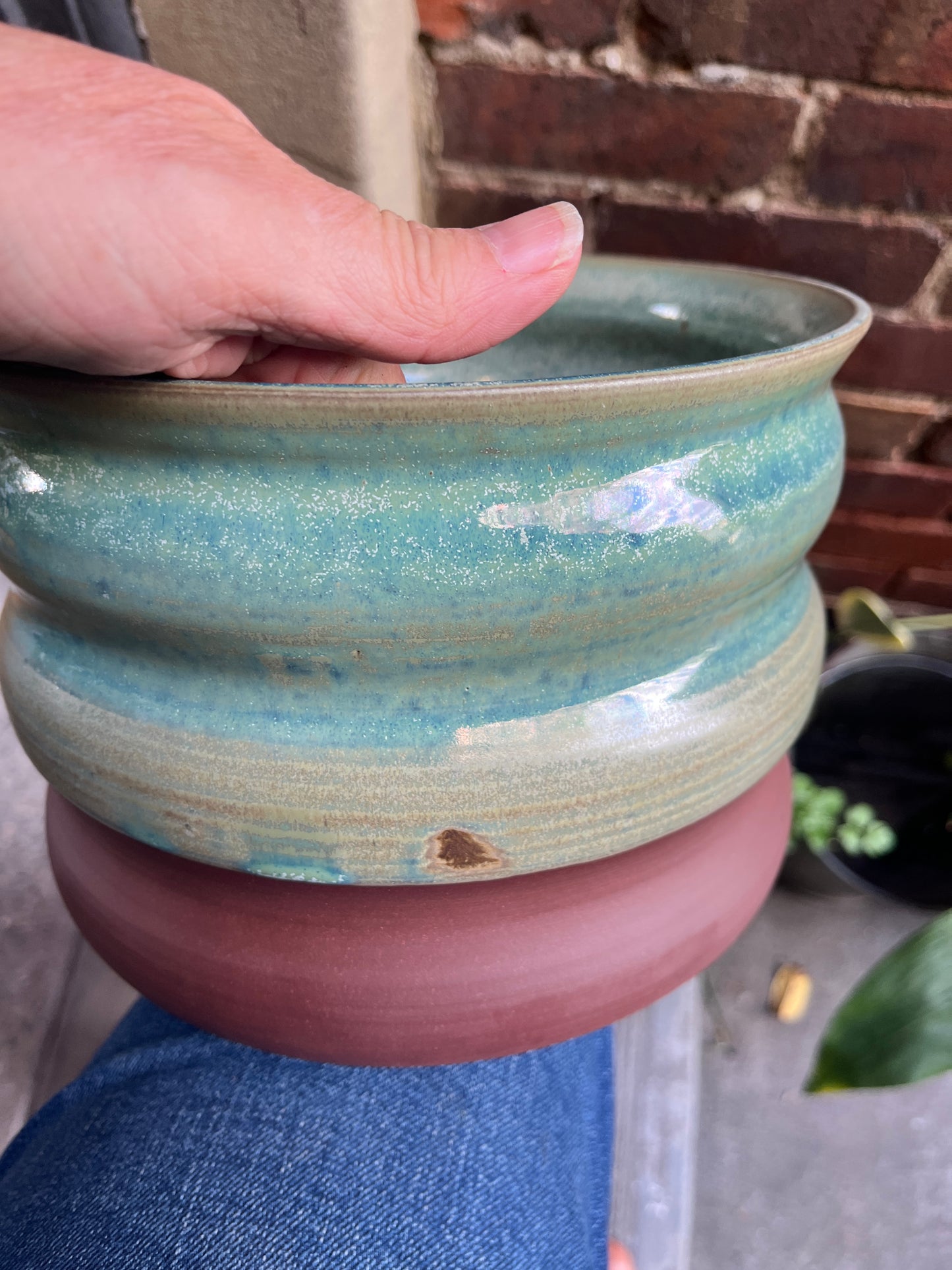 A ceramic planter in variegated shades of green glaze held by a person, with a blurred background