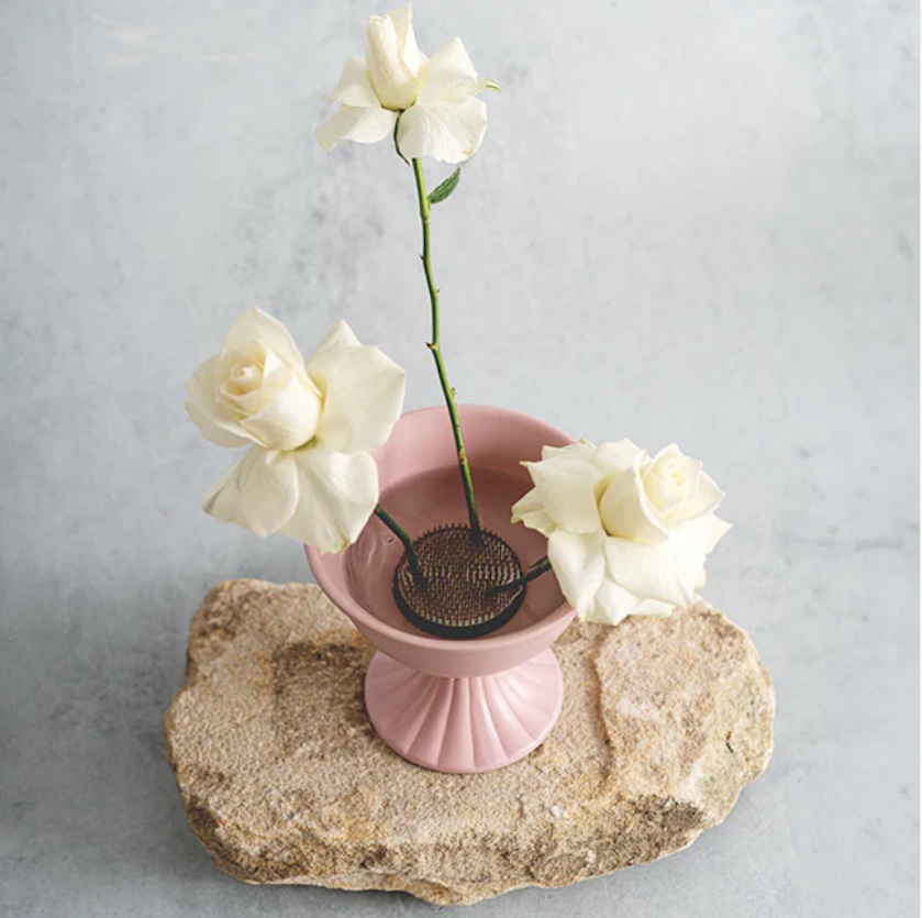 Pink vase with white flowers on a stone surface against a light gray background