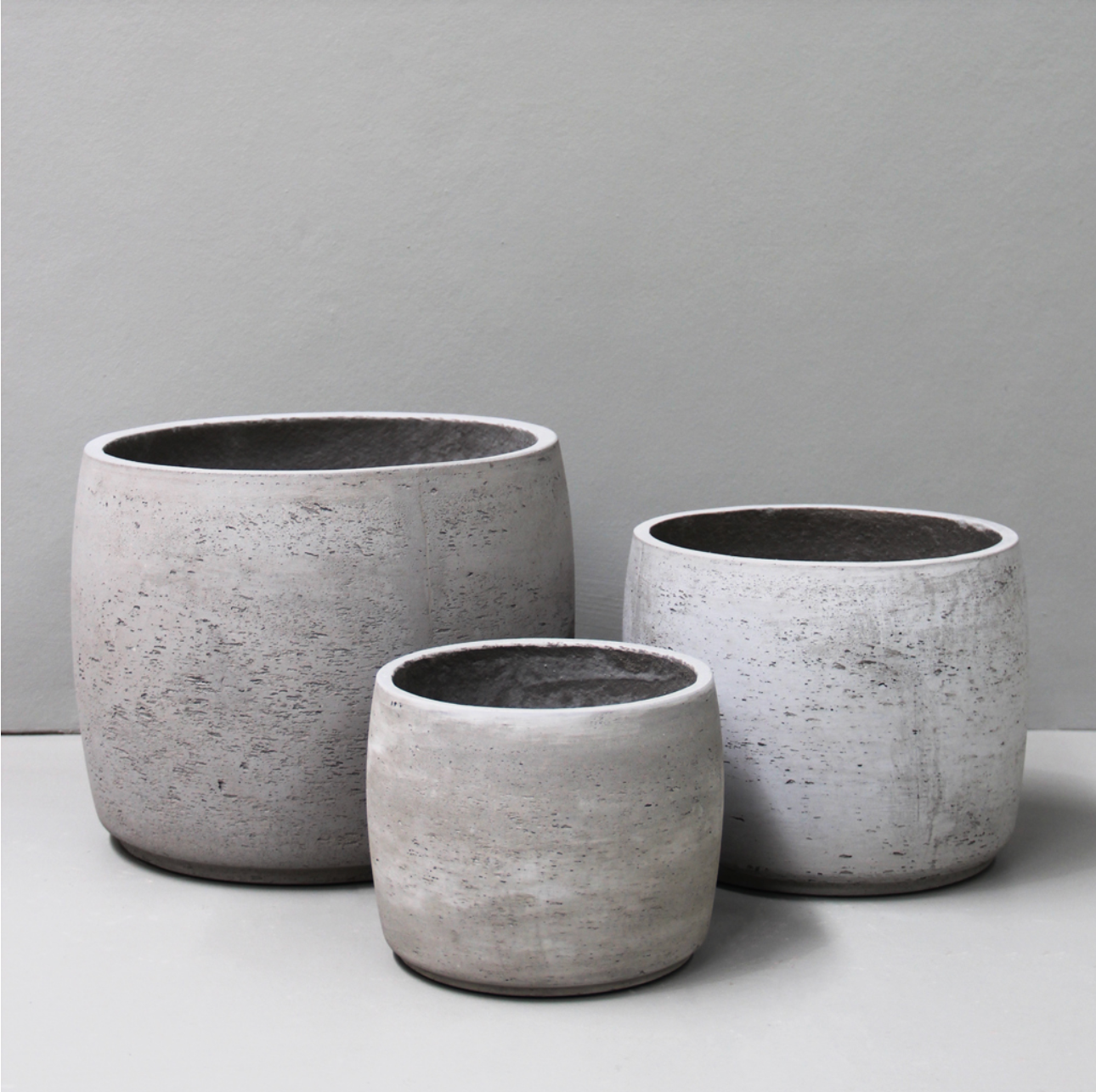 Three gray concrete planters of different sizes on a light gray background