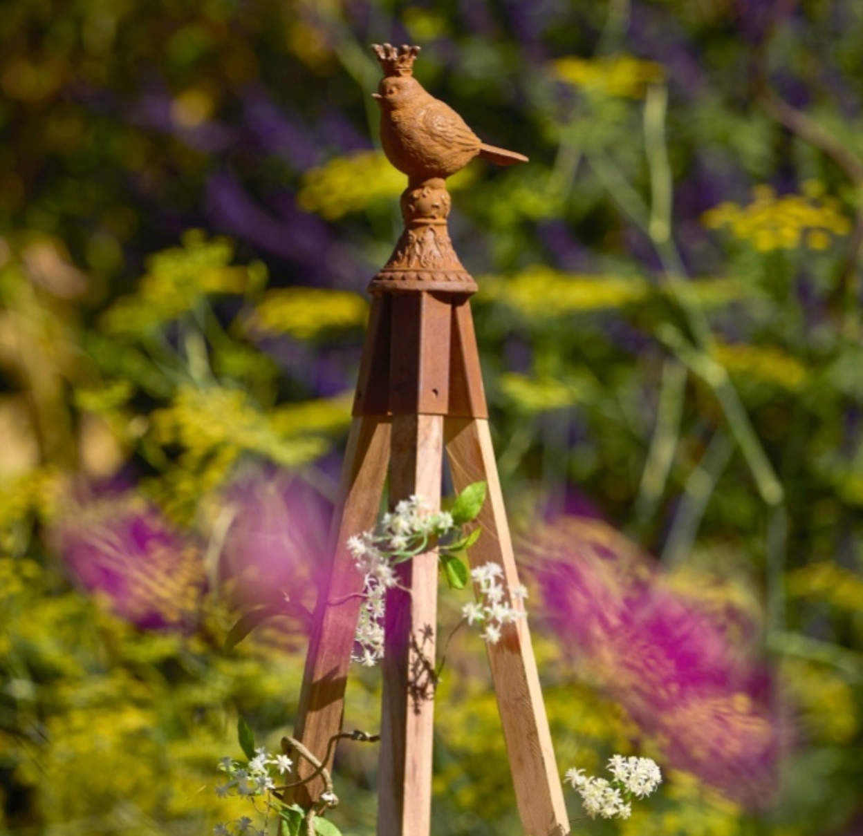 Wooden garden obelisk with bird finial against a blurred garden background