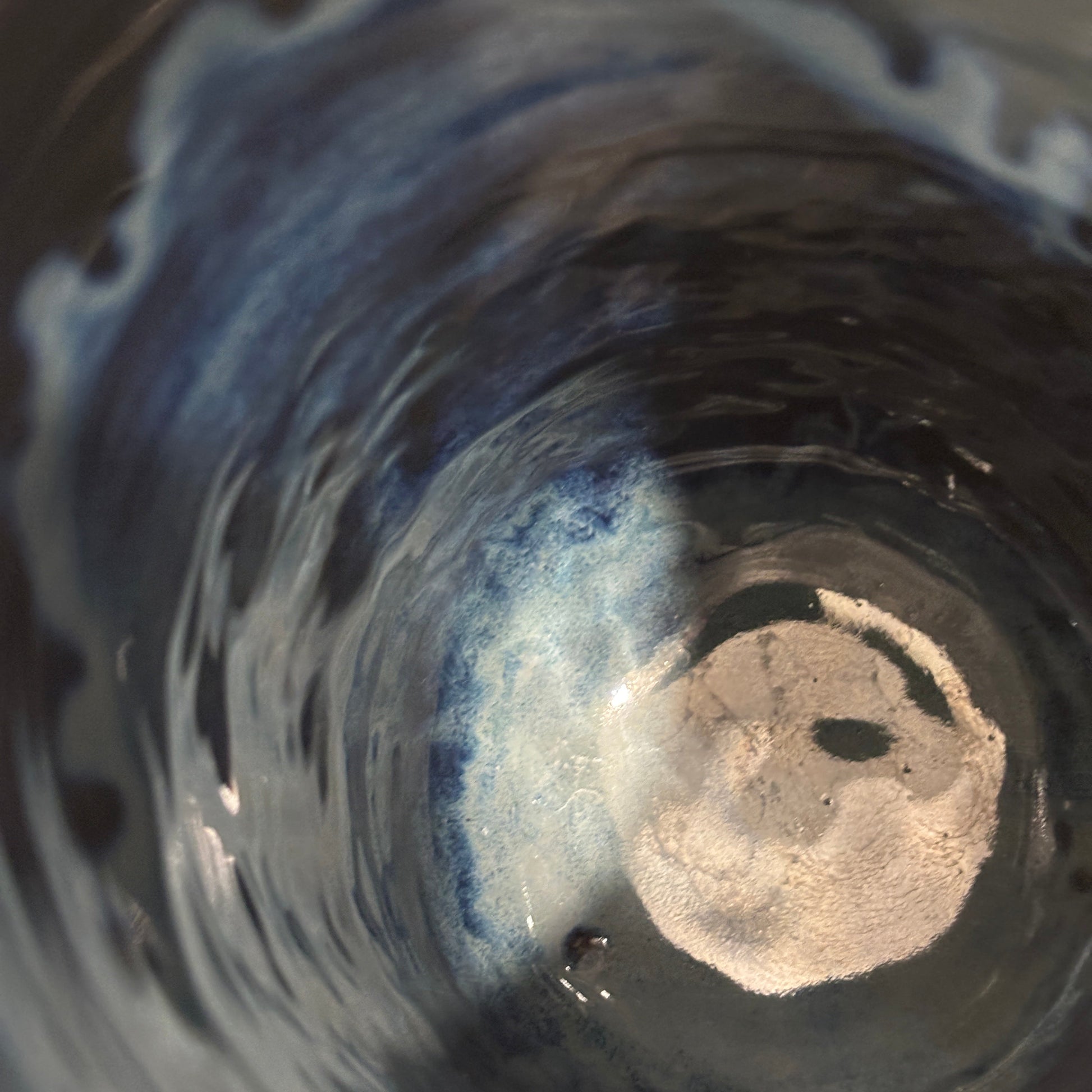 A close-up view inside a dark ceramic vase, showing a light blue and white cloudy liquid swirling at the bottom.