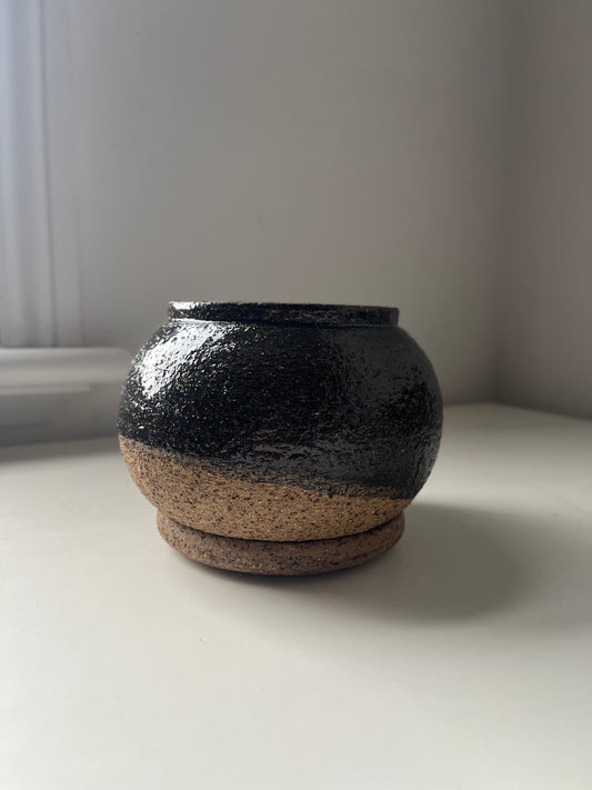 Black ceramic pot on a white surface with a neutral background