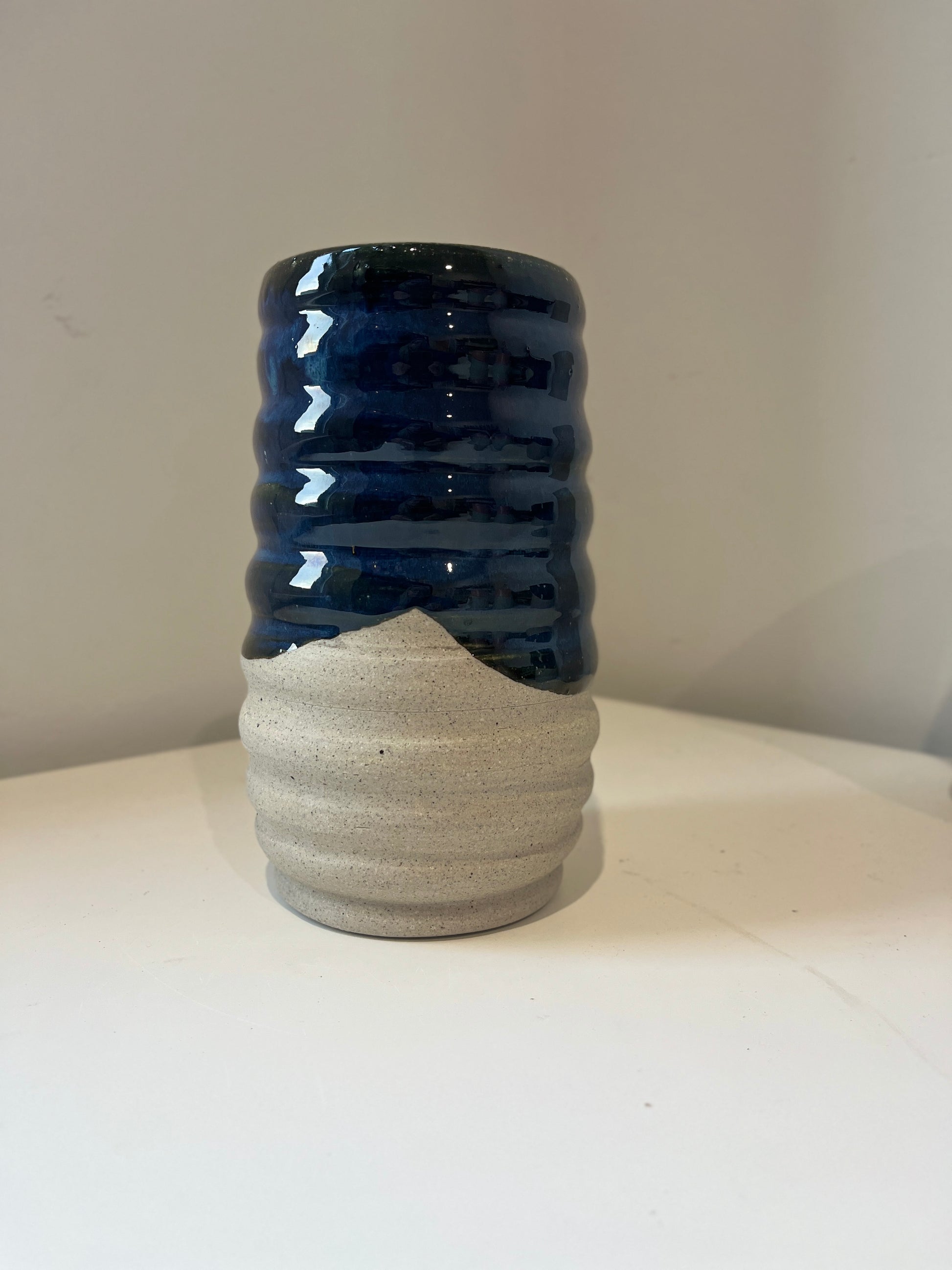 Ceramic vase glazed in dark blue and raw gray speckled clay on a white background.