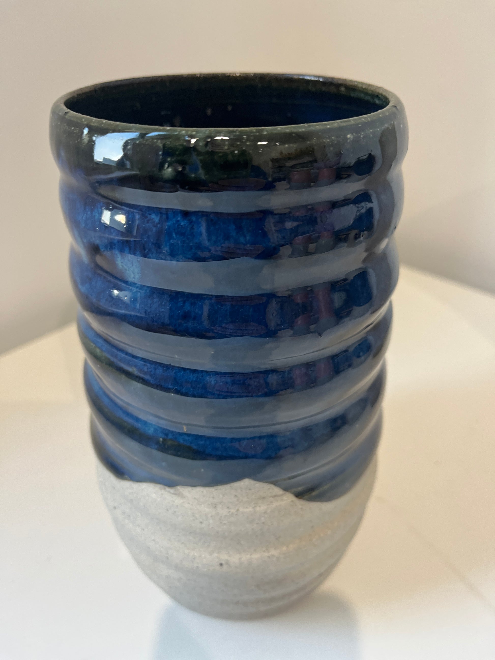 Ceramic vase with blue glaze and raw gray speckled clay on a white surface