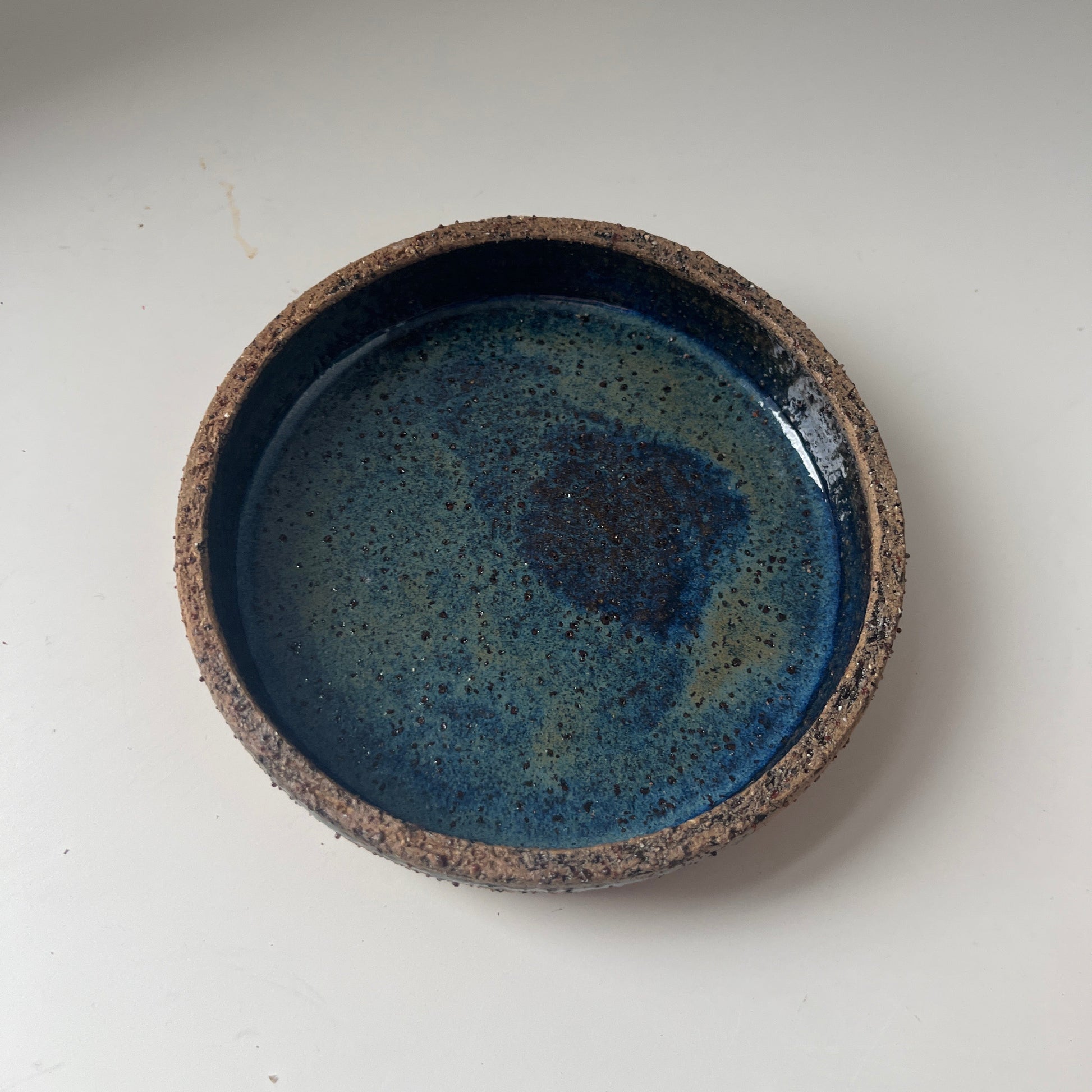 Ceramic saucer with blue glaze and brown rim on a white background