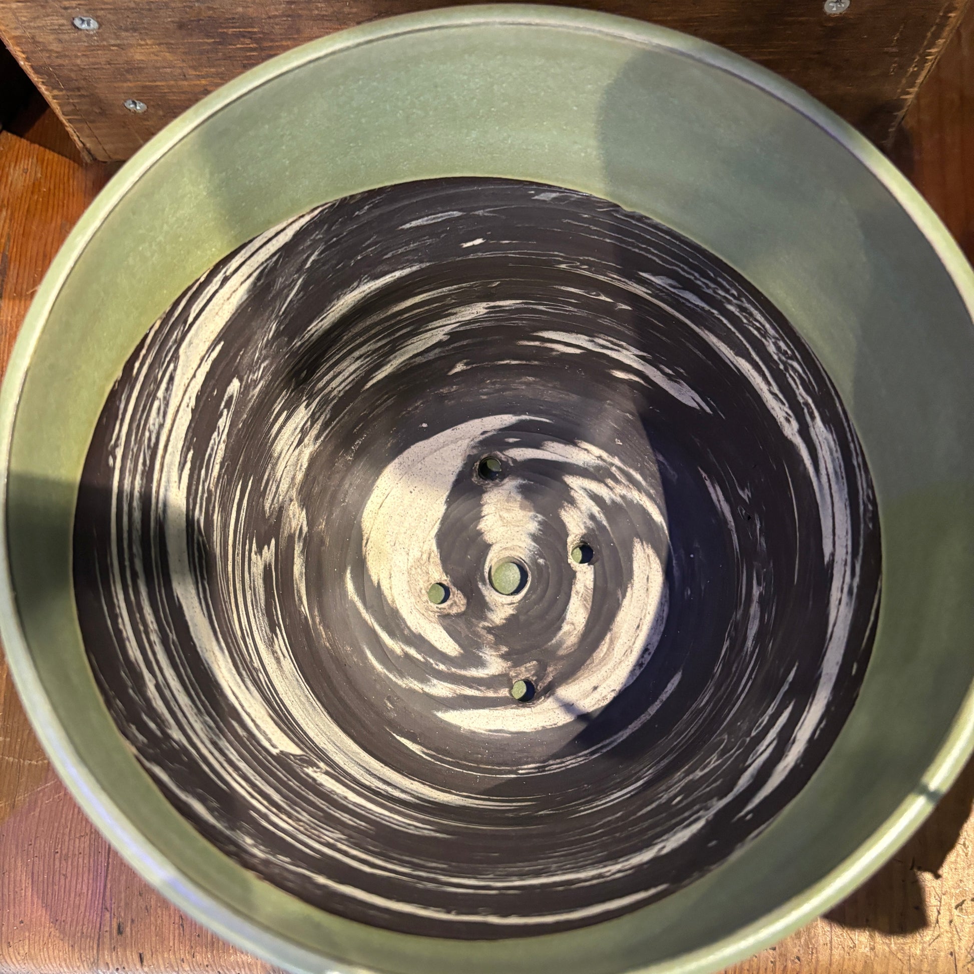 Green ceramic pot with charcoal and cream clay interior on a wooden surface