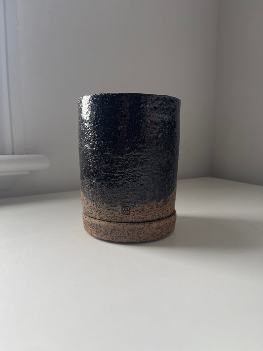 Black and brown cylindrical object against a white wall