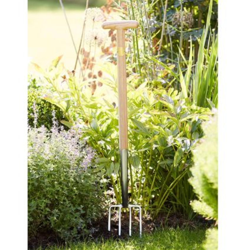 Garden fork standing upright in a garden bed with plants and grass.