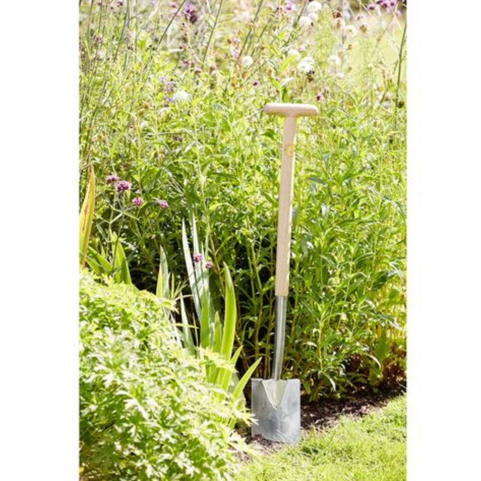 Garden shovel leaning against a grassy and wildflower-covered wall.