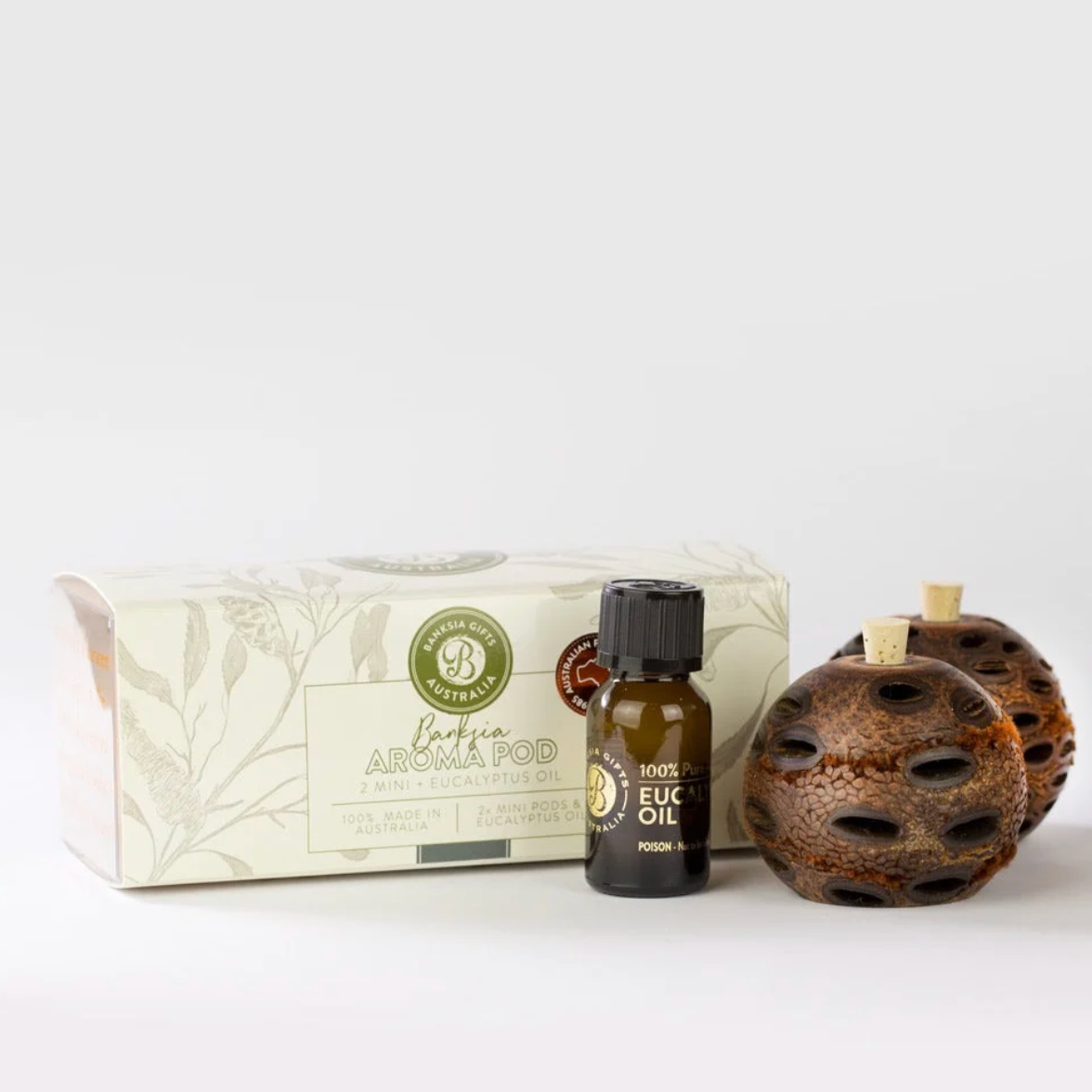 A banksia pod aroma pod kit featuring a white patterned box, a small amber glass bottle of eucalyptus oil, and two brown banksia pod diffusers on a white background.