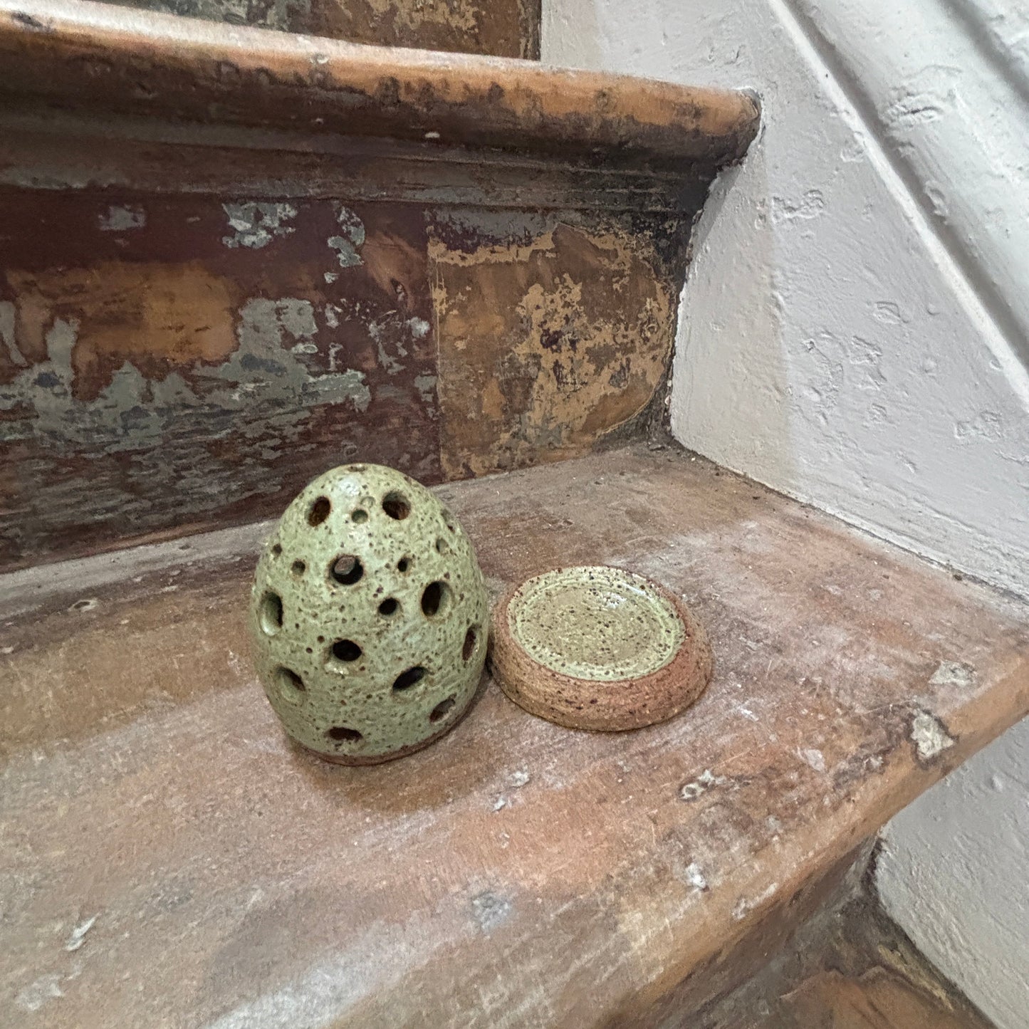 A small handmade ceramic diffuser and matching saucer resting on a rustic wooden staircase.