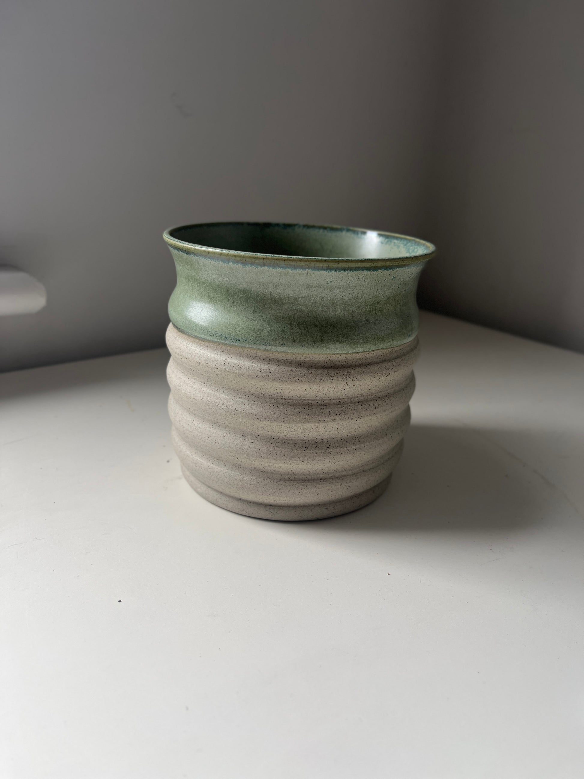 Green ceramic vase on a white surface with a gray background