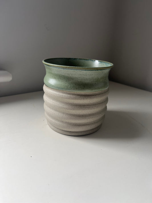 Green ceramic vase on a white surface with a gray background