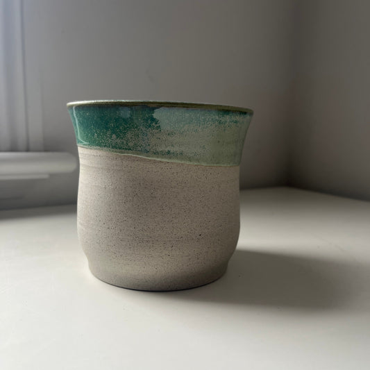 Ceramic planter with green top and raw bottom on a white surface