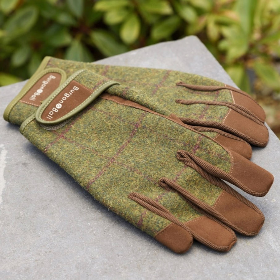 Pair of green and brown gardening gloves on a stone surface with blurred greenery in the background.