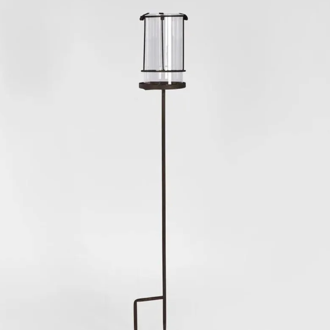 Tall rusty hurricane lamp with a glass shade on a light gray background