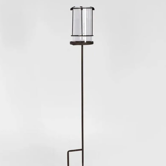 Tall rusty hurricane lamp with a glass shade on a light gray background