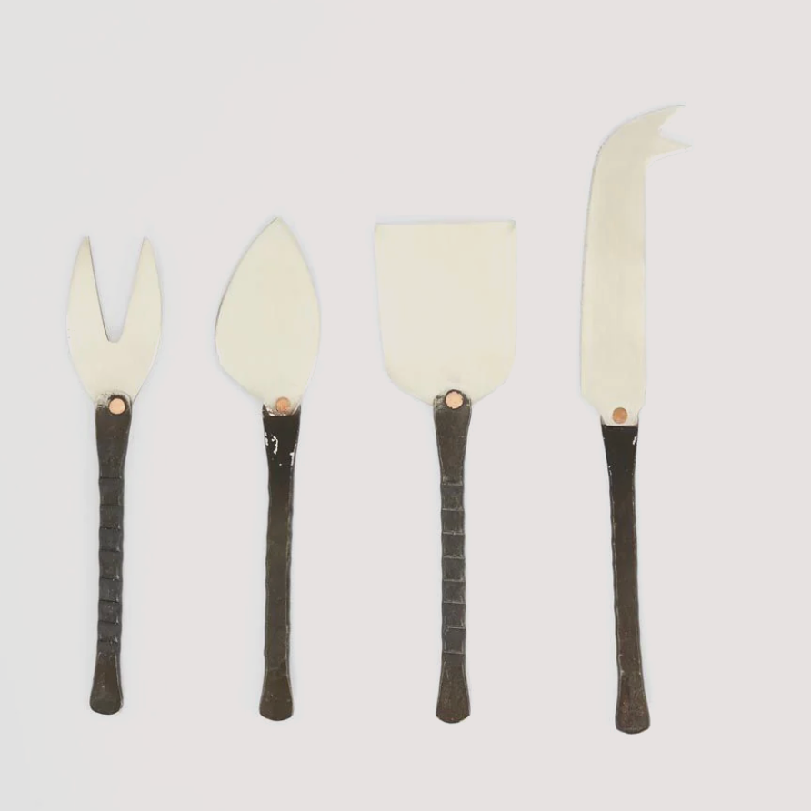 Set of four cheese knives with black handles on a light gray background