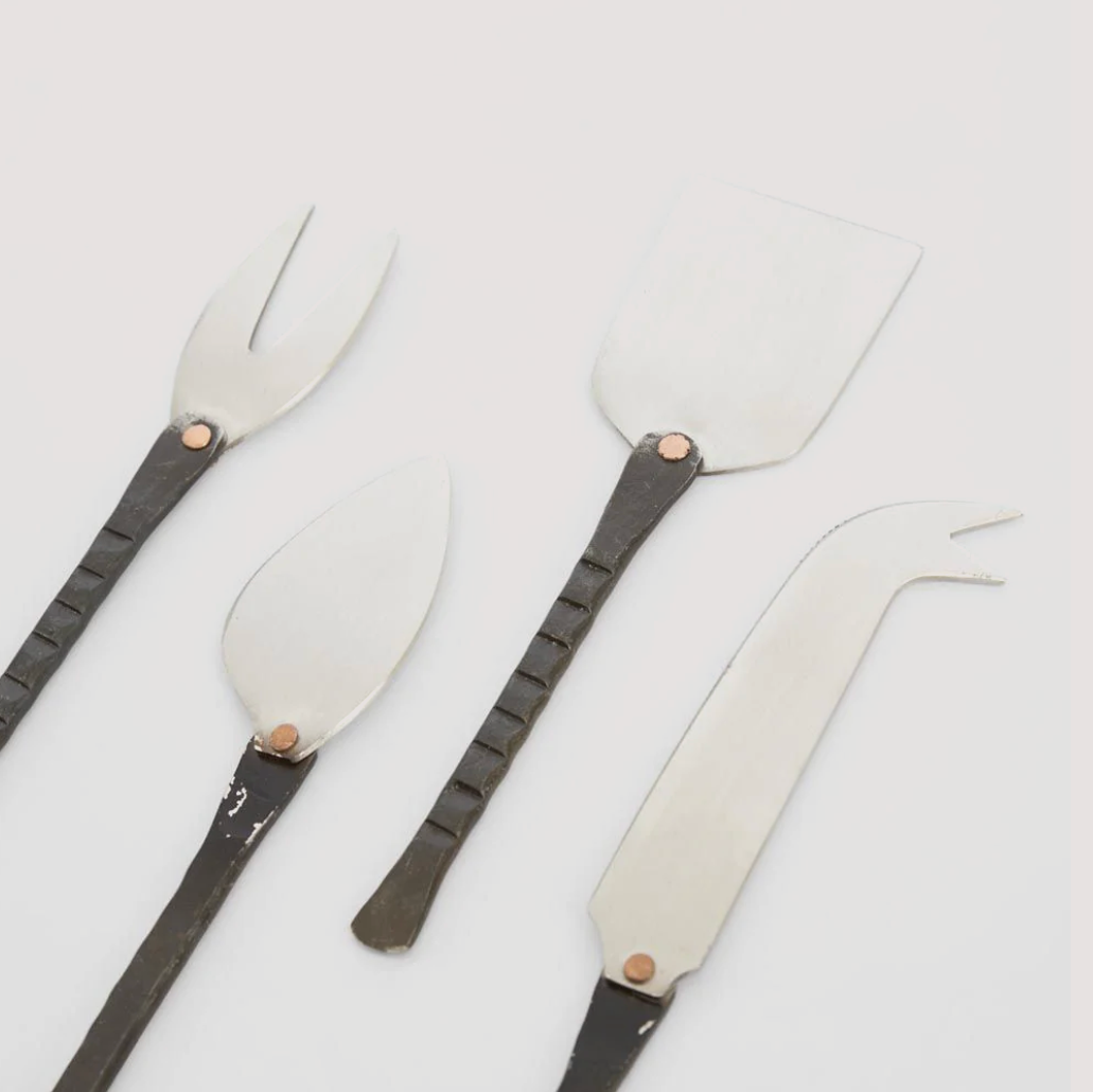 Set of four silver serving utensils with black handles on a light gray background