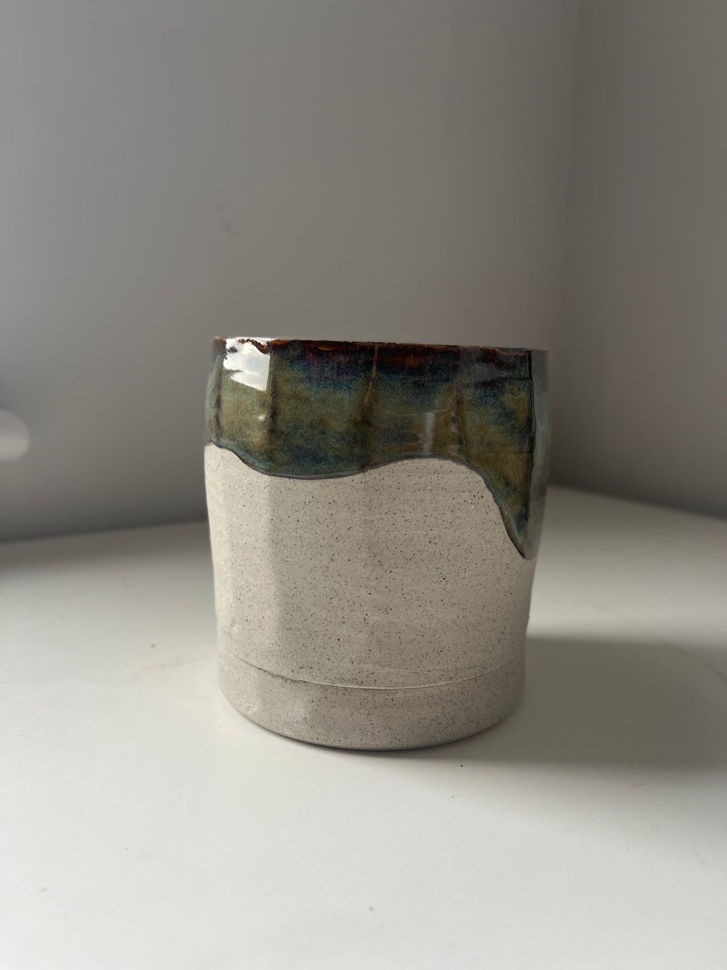 Ceramic planter with a textured surface and greenish top on a white surface.