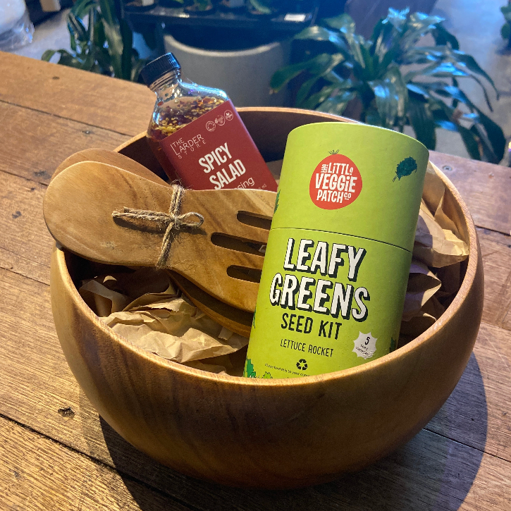 Wooden salad bowl with leafy greens seed kit and salad dressing on a wooden table.
