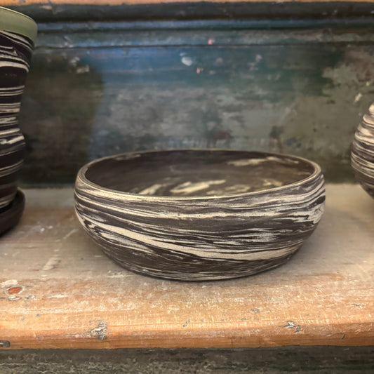 A handmade ceramic bonsai planter with a swirled black and white clay pattern, displayed on a rustic wooden shelf alongside other clay vessels.