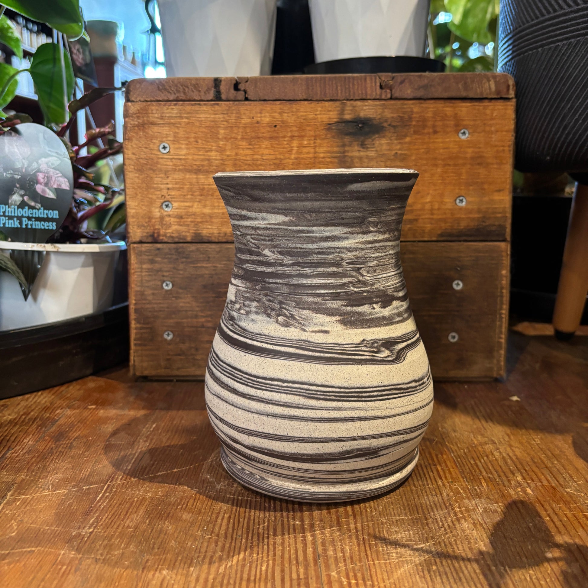 Marbled ceramic vase on a wooden surface with plants in the background
