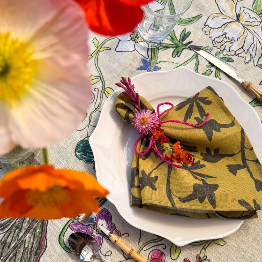 Decorative table setting with a floral napkin, colorful flowers, and a patterned tablecloth.