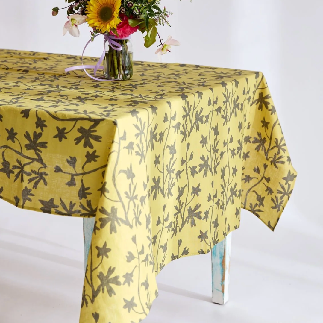 Yellow floral-patterned tablecloth on a white table with a vase of flowers.