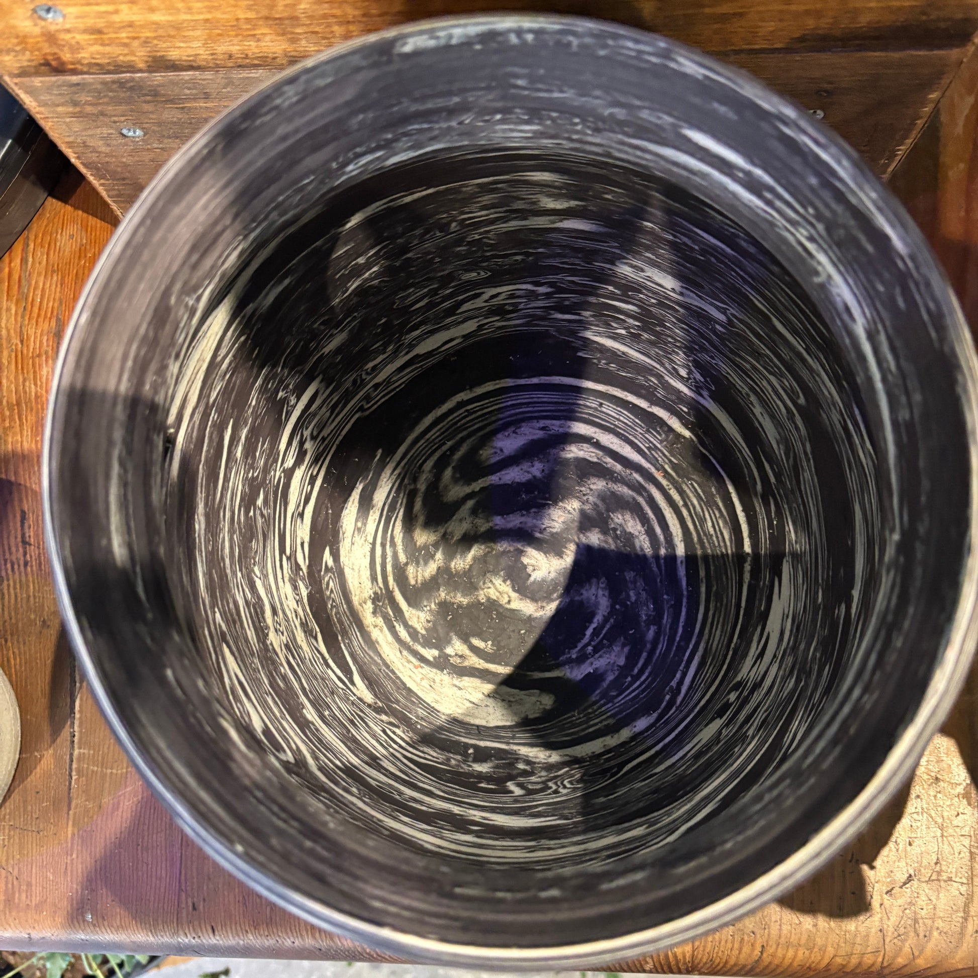 Close-up of a charcoal and cream clay marbled pot with swirling patterns on a wooden surface