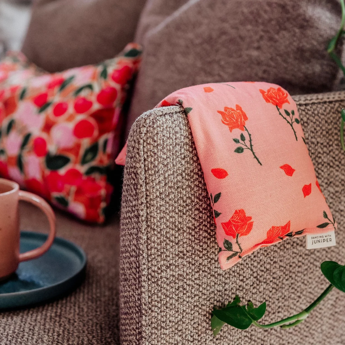 Floral-patterned cushion on a textured sofa with a cup and plant in the background