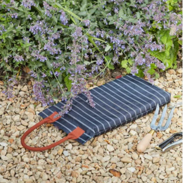 Striped garden kneeler on pebbles with flowers in the background