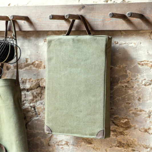 Green fabric garden cushion hanging on a wooden hook against a stone wall.