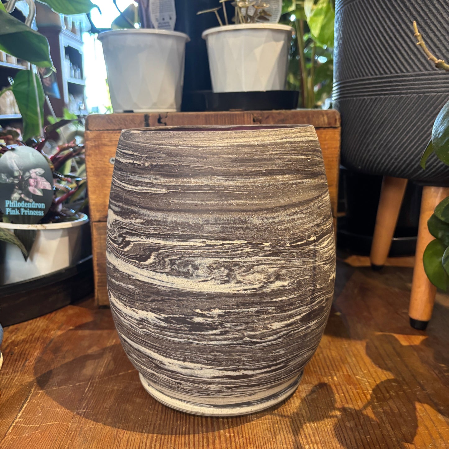 Textured ceramic vase on a wooden surface with plants in the background