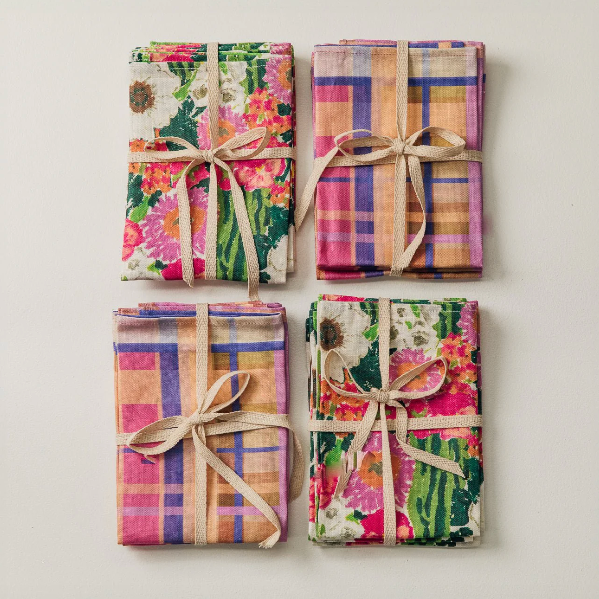 Four folded fabric napkins with floral and plaid patterns tied with ribbons on a light background