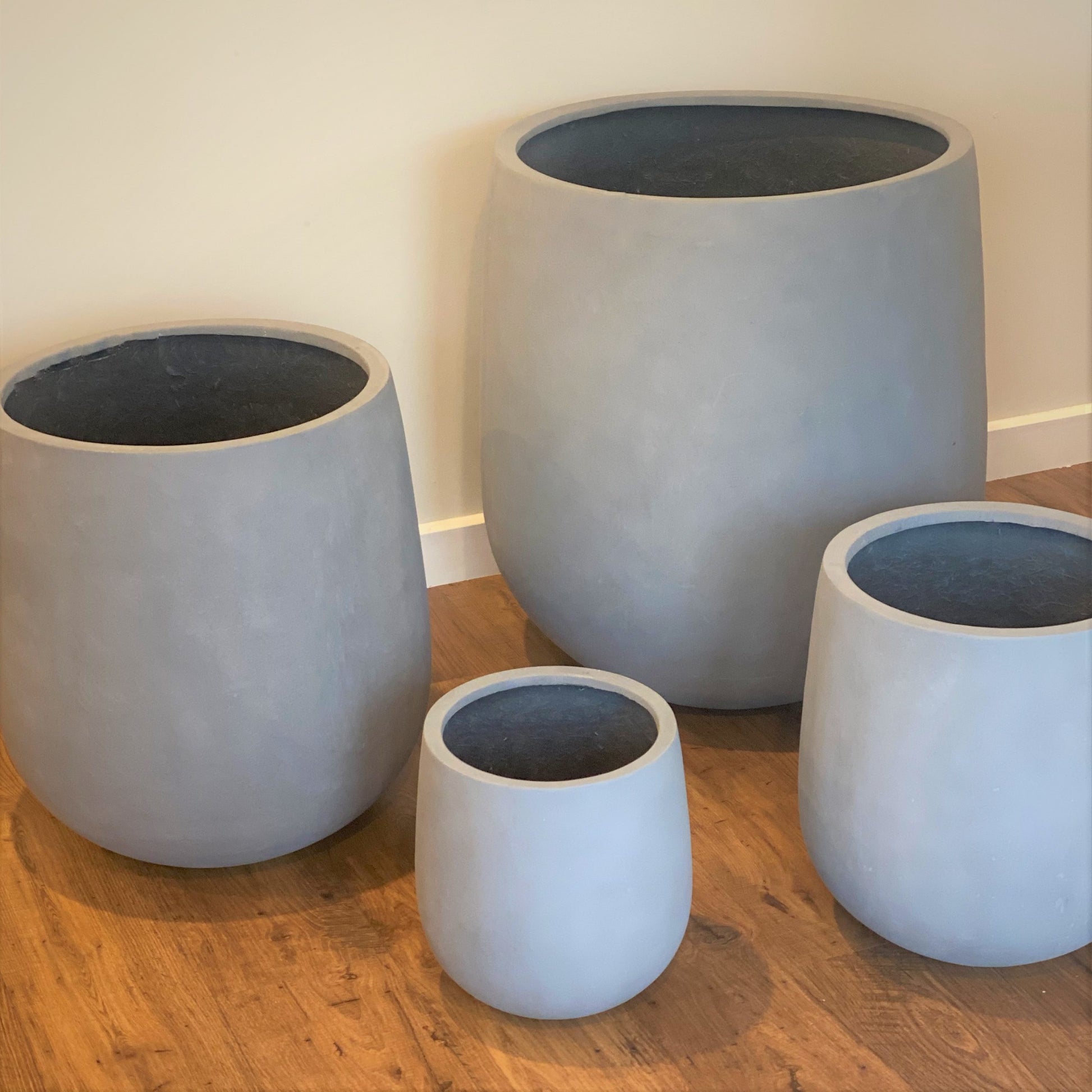 Set of four gray concrete planters on a wooden floor.