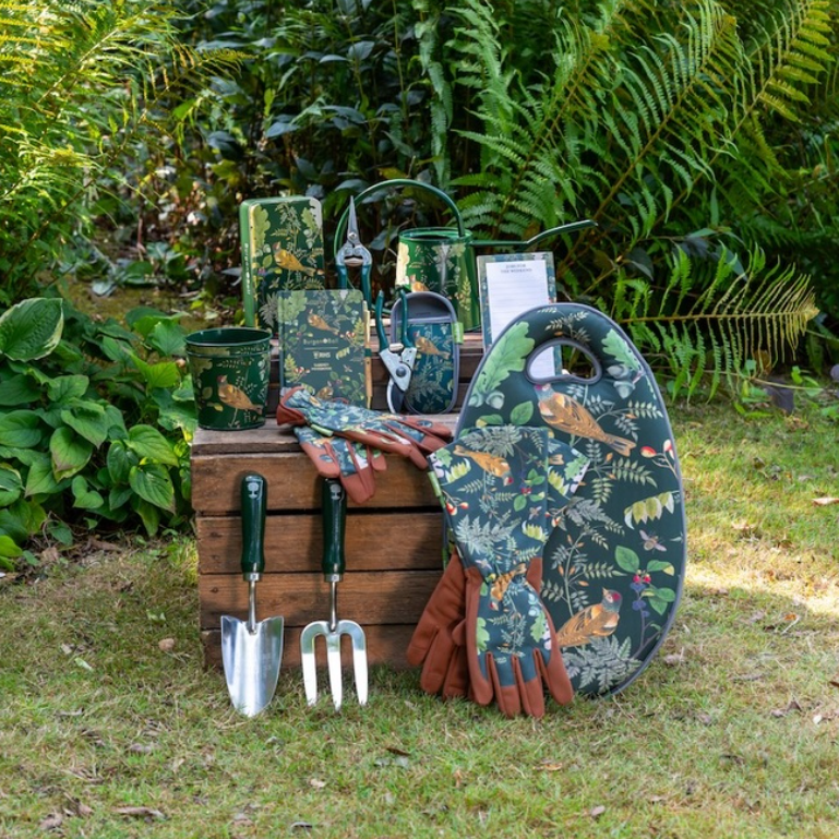 Gardening tools and accessories with a nature-themed design on a wooden crate and wheelbarrow against a garden background.