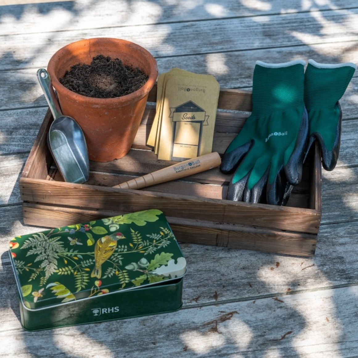 Gardening tools and supplies including a pot, gloves, trowel, and RHS book on a wooden surface.