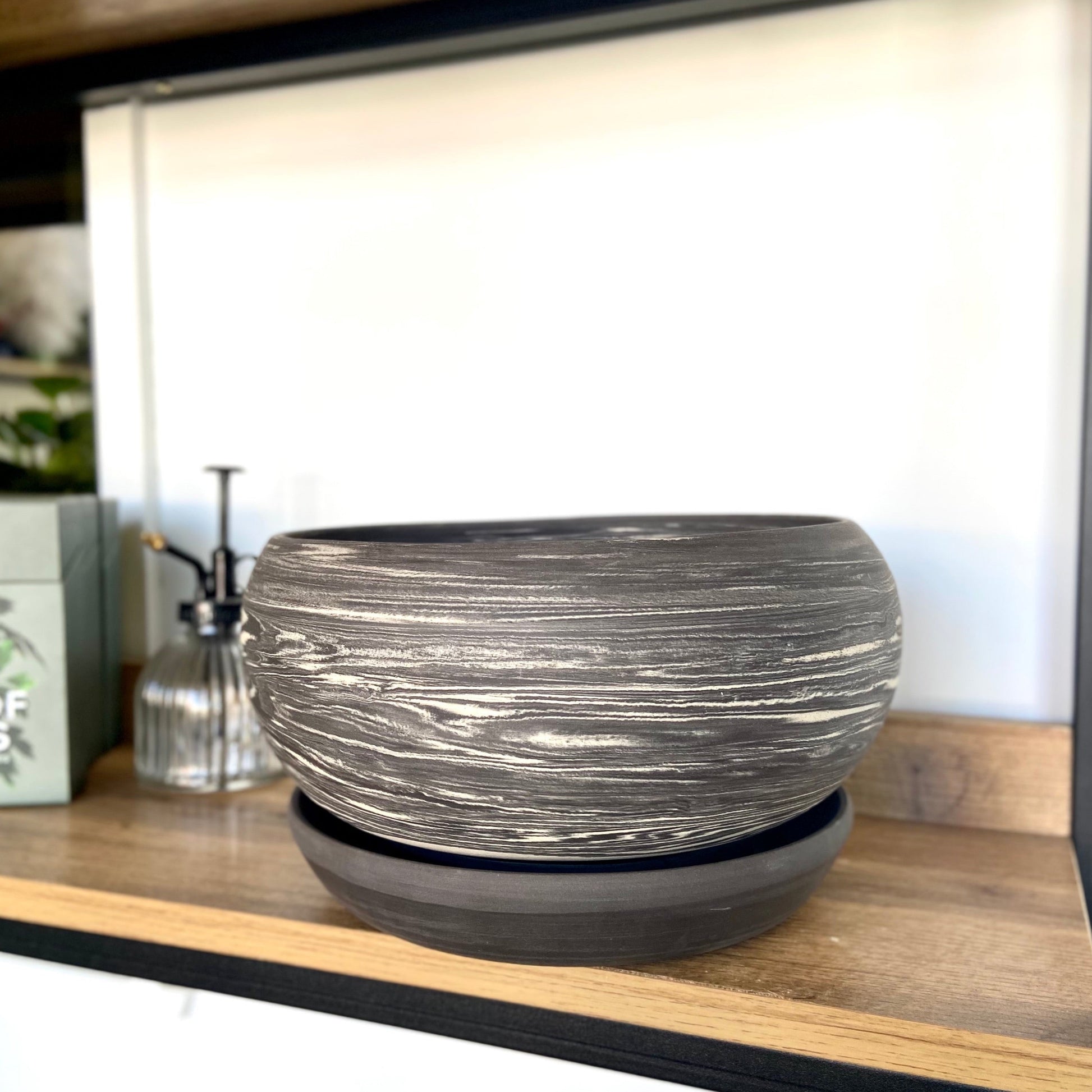 A black and white marbled ceramic planter with a drainage hole, placed on a wooden surface.